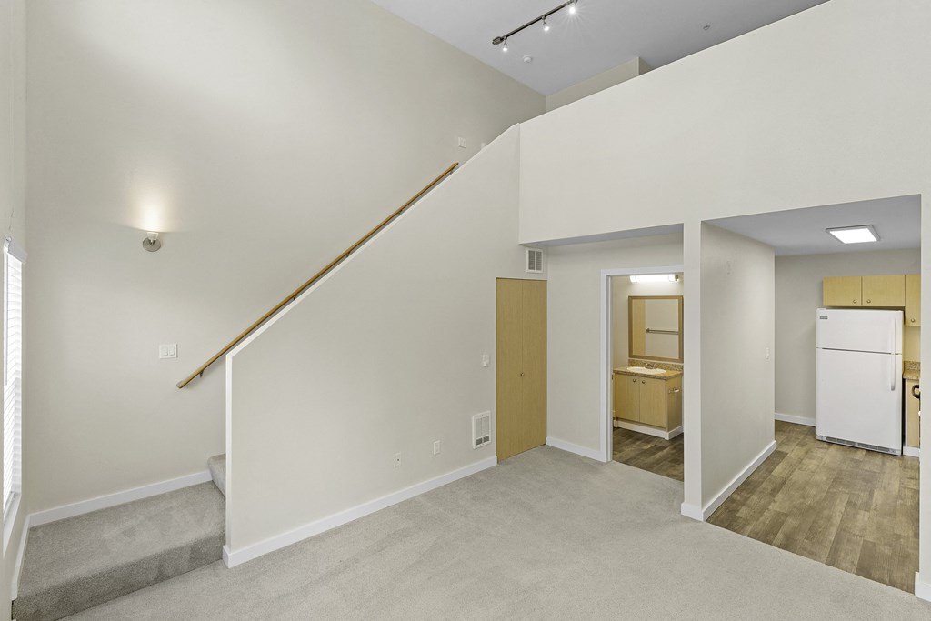 Loft-Style Apartment with Sconce Lighting Up Stairs to Living Area, Plush Carpeting, and Kitchen View in the Background Loft-Style Apartment with Sconce Lighting Up Stairs to Living Area, Plush Carpeting, and Kitchen View in the Background at Sir Gallahad Apartment Homes, Bellevue